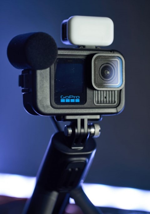 Közeli kép a GoPro HERO13 Black kameráról Creator Edition összeállításban: Media Mod keret, szivacsos szélfogóval ellátott külső mikrofon és világító LED lámpa az akciókamerán, állványra rögzítve.
