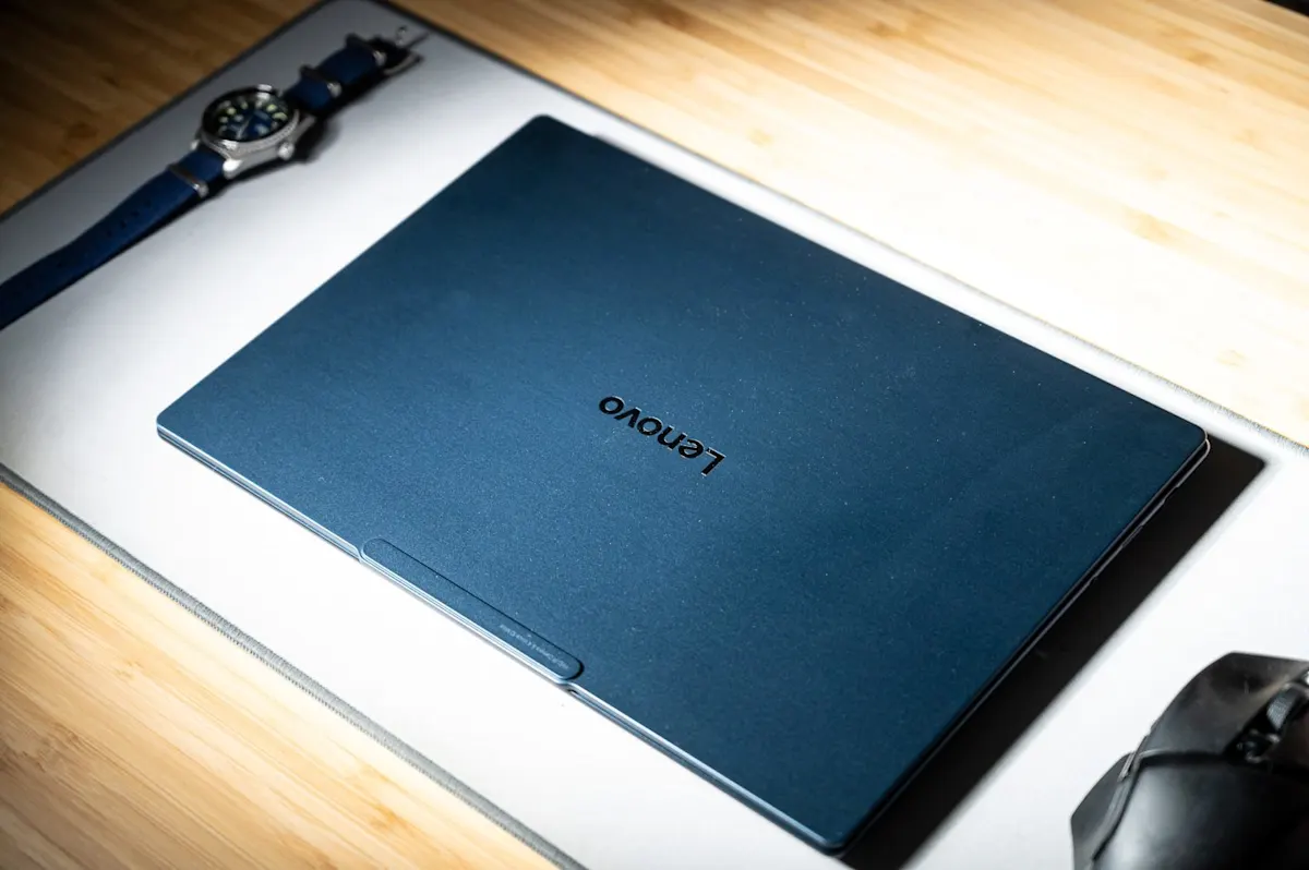 Lenovo Yoga Slim 7x laptop sötétkék fedlapja Lenovo logóval egy íróasztalon.