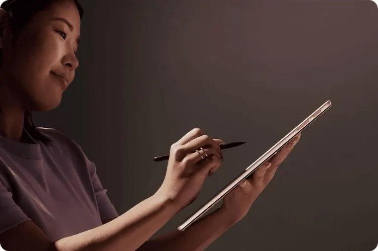 Nő tart egy táblagépet, és egy fekete tollal ír rá a sötét háttér előtt.