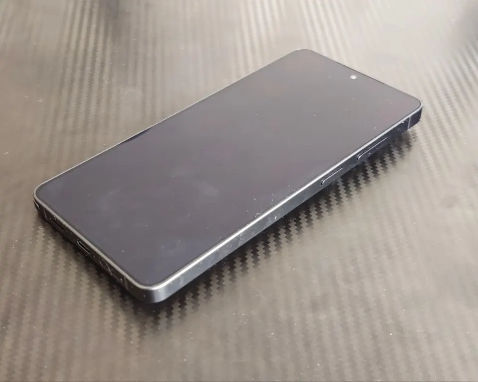 Kikapcsolt kijelzőjű Samsung Galaxy S24 Ultra okostelefon fektetve, karbon mintás felületen.