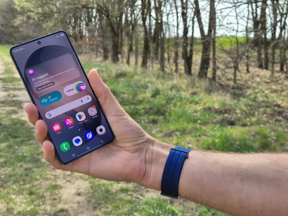 Samsung Galaxy S24 Ultra okostelefon kijelzője és kezdőképernyője kézben tartva a szabadban.