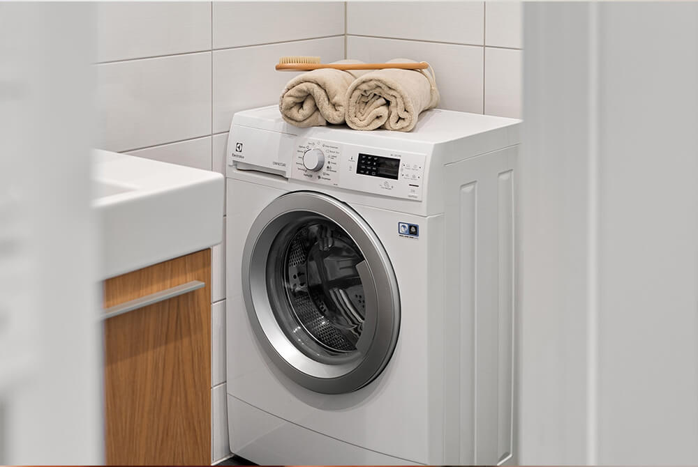 Fehér mosógép, rajta "Eco Cycle" felirat, gombok és egy kéz beállítja a programot.