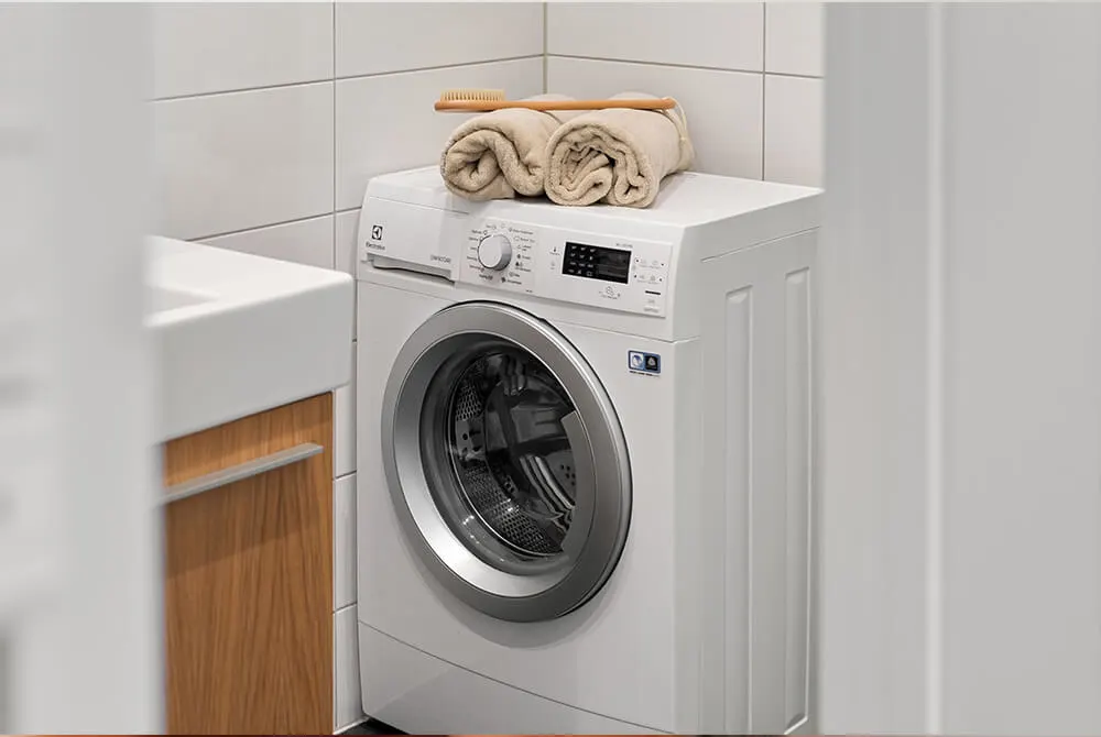Fehér mosógép, rajta "Eco Cycle" felirat, gombok és egy kéz beállítja a programot.