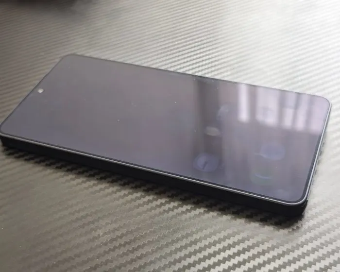 Kikapcsolt kijelzőjű Samsung Galaxy S24 Ultra okostelefon lapos szögben fektetve, karbon mintás felületen.