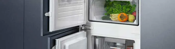 Nyitott hűtőszekrény zöldségekkel, spárgával és gyümölcsökkel. A hűtőszekrény a konyhai szekrénybe van beépítve.