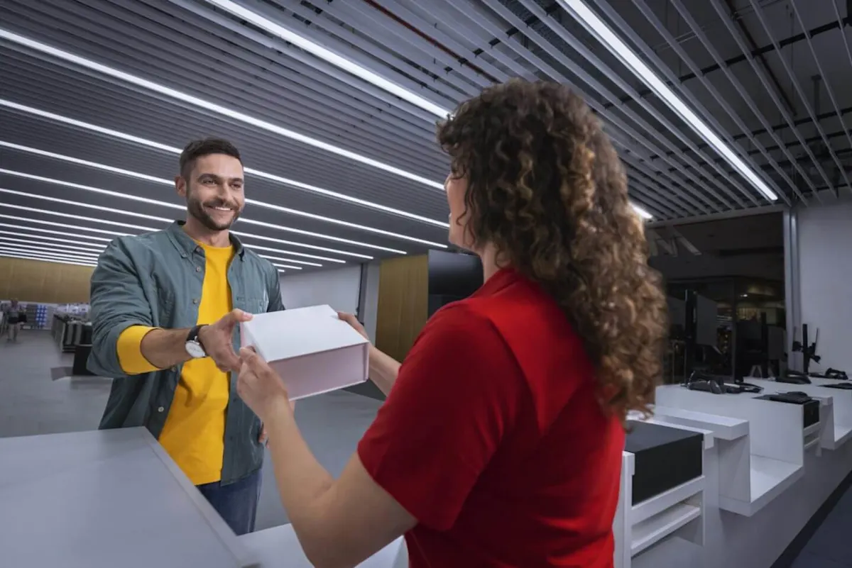 Vásárló átvesz egy dobozt a MediaMarkt eladójától az üzletben, modern belső térben.