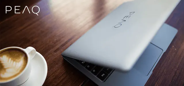 Fa asztalon kávéscsésze és részben nyitott laptop látható. A laptop fedelén a PEAQ felirat olvasható.