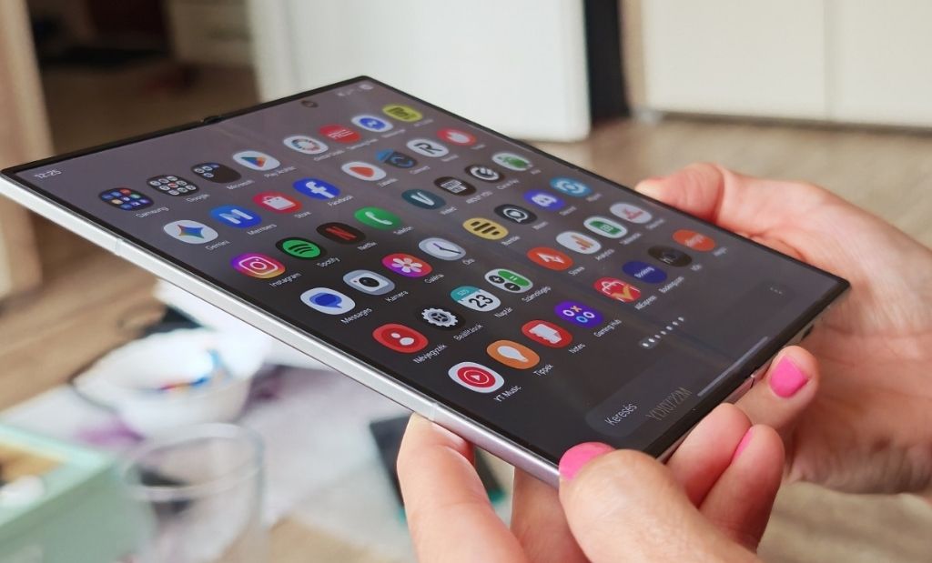 Kihajtott Samsung Galaxy Z Fold okostelefon kézben tartva, alkalmazáslistát megjelenítő nagy belső kijelzővel.