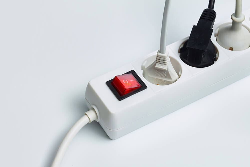 Fehér hosszabbító piros kapcsolóval. Két csatlakozóba dugó van bedugva: egy fehér és egy fekete.