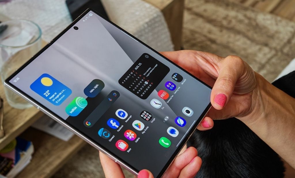 Kézben tartott, kihajtott Samsung Galaxy Z Fold okostelefon bekapcsolt belső kijelzővel és alkalmazásikonokkal