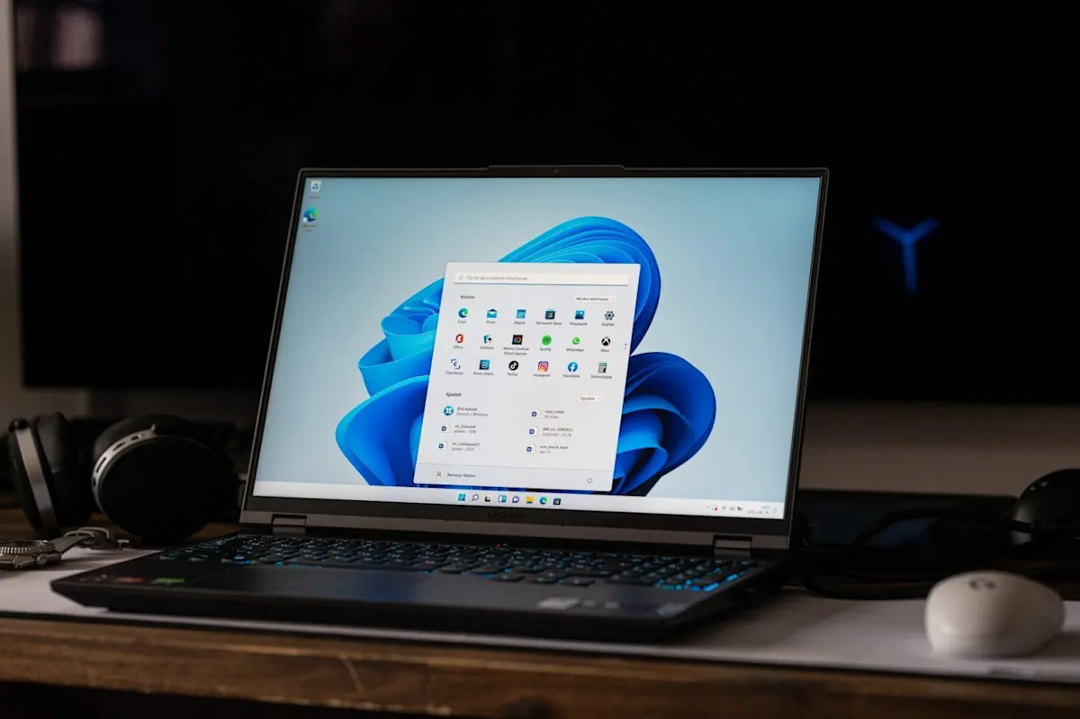 Bekapcsolt Lenovo Legion laptop az asztalon, világító billentyűzettel és a kijelzőn megnyitott Windows 11 Start menüvel.