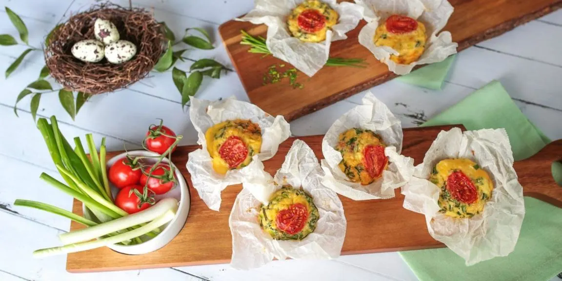Zöldséges-sonkás frittata falatkák koktélparadicsommal, sütőpapírban elrendezve deszkán.   