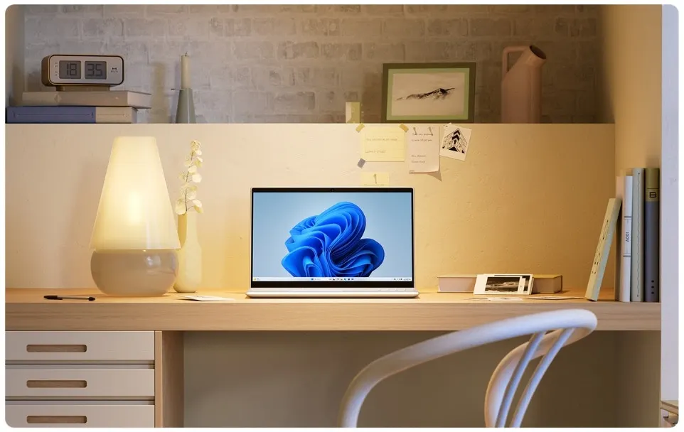 Íróasztal lámpával, laptop Windows 11 háttérrel, papírokkal és könyvekkel, székkel egy szobában.