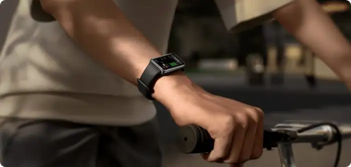 Közeli felvétel egy kerékpározó személy karjáról, akinek csuklóján egy fekete szíjas Huawei Watch Fit 3 okosóra látható, miközben a kezével a kormányt fogja.