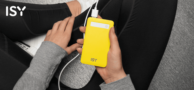 A képen egy sárga ISY power bank látható, mely egy szürke felsőt és fekete nadrágot viselő személy kezében van. Egy fehér töltőkábel csatlakozik hozzá.