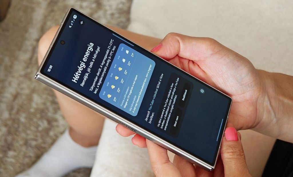 Kézben tartott Samsung Galaxy Z Fold okostelefon bekapcsolt külső kijelzővel, időjárás-előrejelzést megjelenítő alkalmazással.