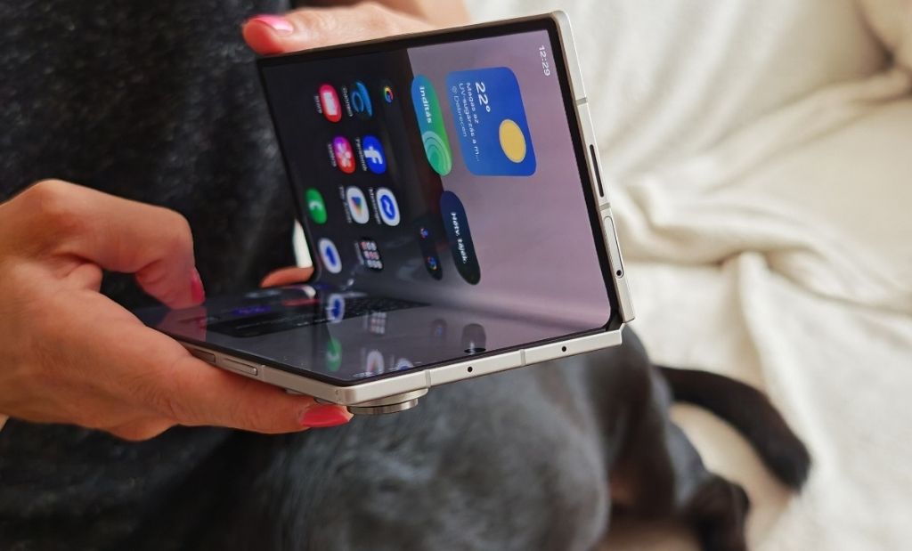 Félig kihajtott Samsung Galaxy Z Fold okostelefon kézben tartva, bekapcsolt kijelzővel és látható zsanérral
