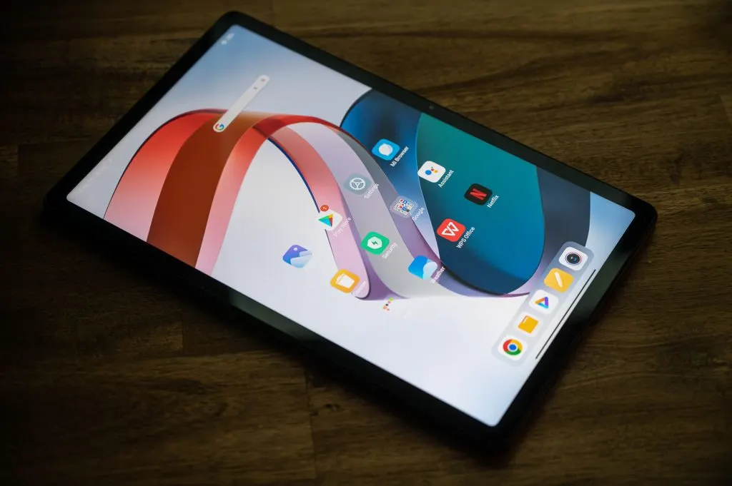 Bekapcsolt Redmi Pad táblagép színes gyári háttérképpel és alkalmazásikonokkal a kijelzőjén, egy sötét fa asztalra helyezve.