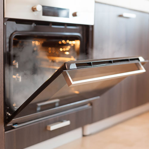 Konyhai környezetben egy nyitott sütő látható, benne fény és gőz, a konyhaszekrény részletei látszanak a háttérben.