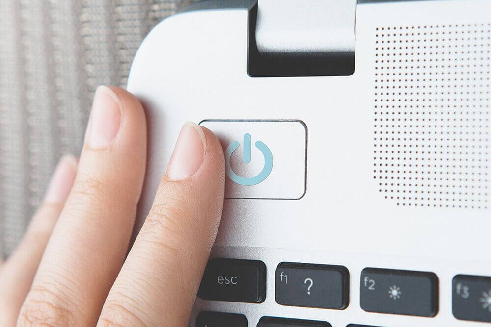 Egy kéz nyomja meg a fehér laptop bekapcsológombját, melynek közelében fekete billentyűk találhatók.