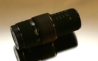 Fényképezőgép objektív fekszik egy fényvisszaverő felületen, világos háttér előtt.