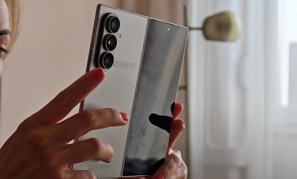 Kihajtott Samsung Galaxy Z Fold okostelefon kézben tartva, látható háromkamerás hátlapi kialakítással és nagy belső kijelzővel.