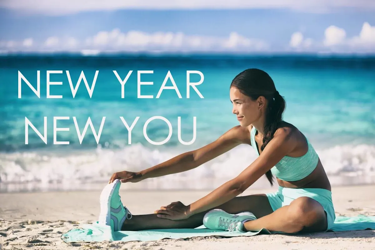 Sportos nő nyújtózkodik a tengerparton jógamatracon, háttérben az óceán és „New Year New You” felirat – újévi fogadalom és fitnesz.