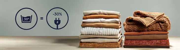 Két halom összehajtott ruhát mutat a kép. Balra mosási (30fok) és energiatakarékossági ikonok (-30% felirat) láthatók.