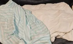 Gyűrött fehér és csíkos ágyneműk egy kupacban a szárítás utáni vasalás előtt.