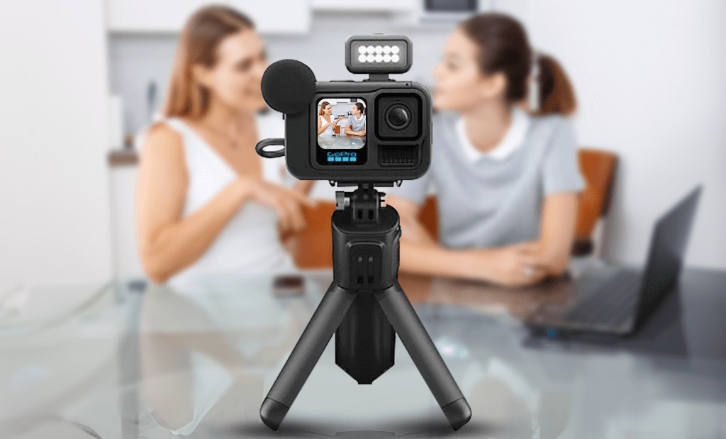 GoPro HERO13 Black Creator Edition csomag: az akci ókamera állványra rögzítve, kiegészítő lámpával és külső mikrofonnal felszerelve, a háttérben két homályos női alakkal egy asztalnál.