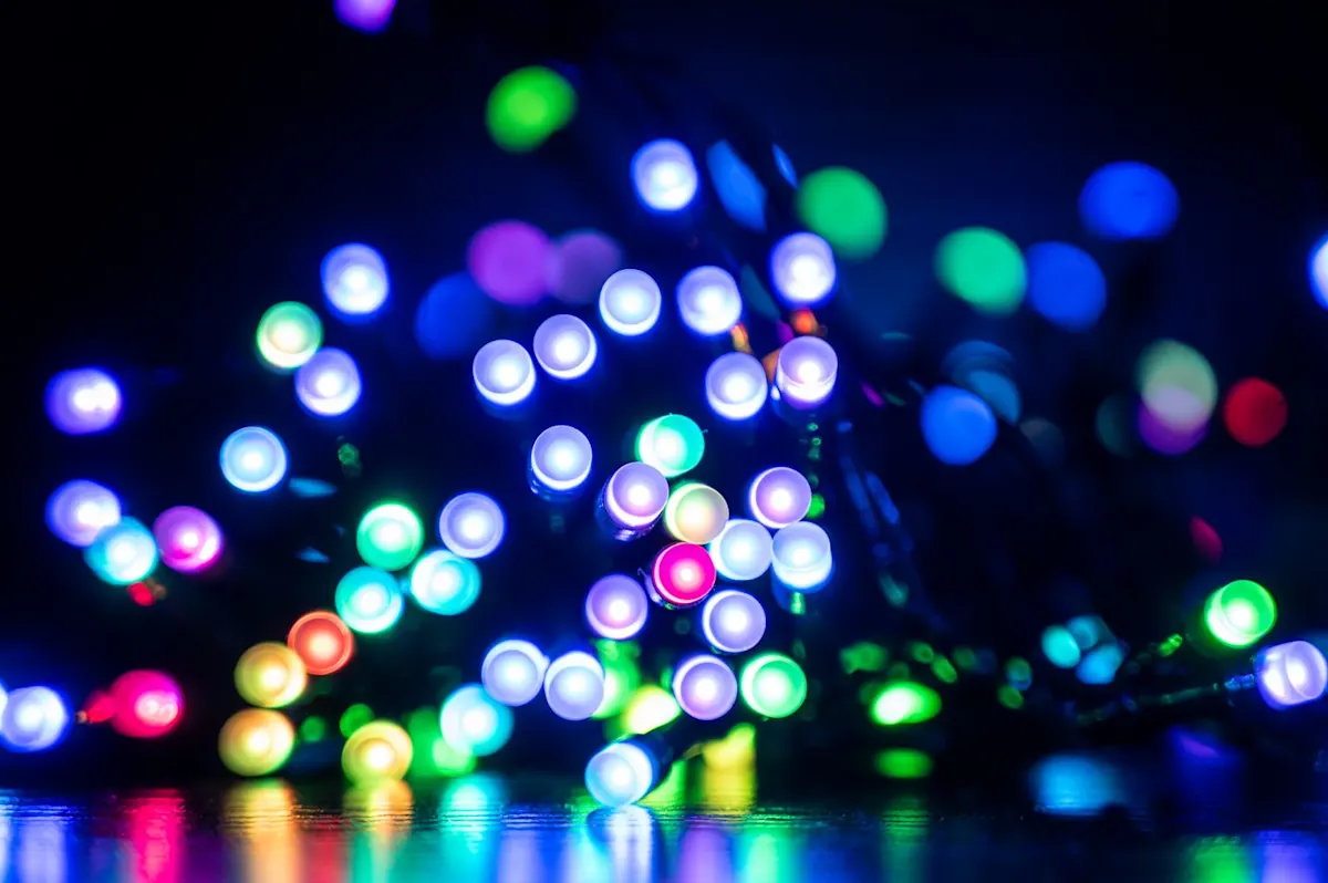 Színesen világító karácsonyi LED fényfüzér közelről, sötét háttérrel és elmosódott háttérfényekkel (bokeh hatással).