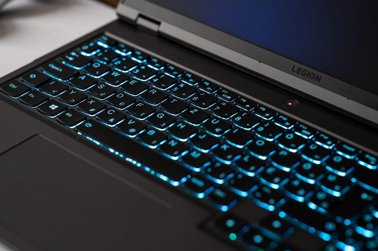 Lenovo Legion laptop billentyűzete élénk kék háttérvilágítással, felette a bekapcsológombbal és a képernyőkeret alsó részével.