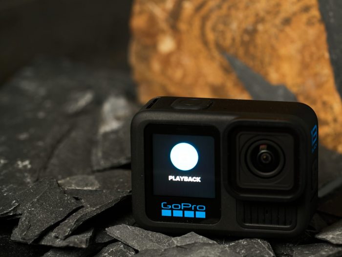 GoPro HERO13 Black akciókamera fekete palaköveken, az előlapi kijelzőjén a 'PLAYBACK' felirattal és egy fehér kör ikonnal, a háttérben barna kőzettel.
