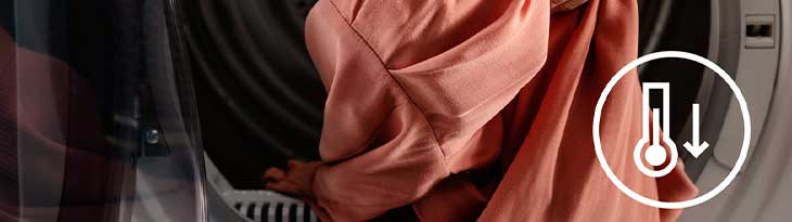 Egy személy rózsaszín ruhát tesz egy mosógépbe, melyen egy hőmérsékletet jelző ikon látható.
