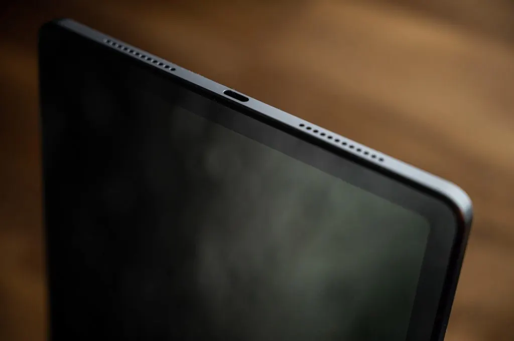 Közeli fotó egy táblagép felső éléről, amelyen az USB-C csatlakozó és a két oldalsó hangszórórács látható, sötét, elmosódott háttérrel.