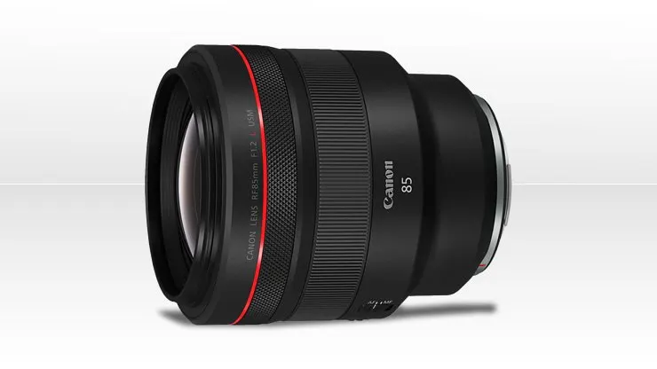 Egy zömök, fekete színű Canon RF 85mm F1.2 L USM fix objektív, elülső részén jellegzetes piros csíkkal, világos háttér előtt elhelyezve