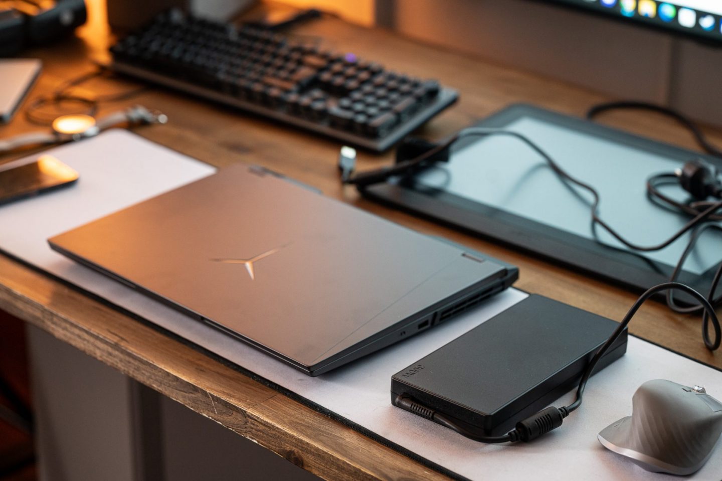 Zárt, sötétszürke Lenovo Legion laptop egy íróasztalon, mellette fehér kontrollerrel, egérrel, fejhallgatóval és egy karórával.