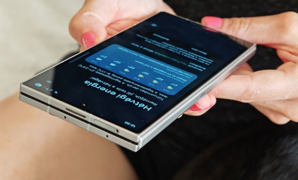Összecsukott Samsung Galaxy Z Fold okostelefon kézben tartva, bekapcsolt külső kijelzővel oldalnézetből fotózva.