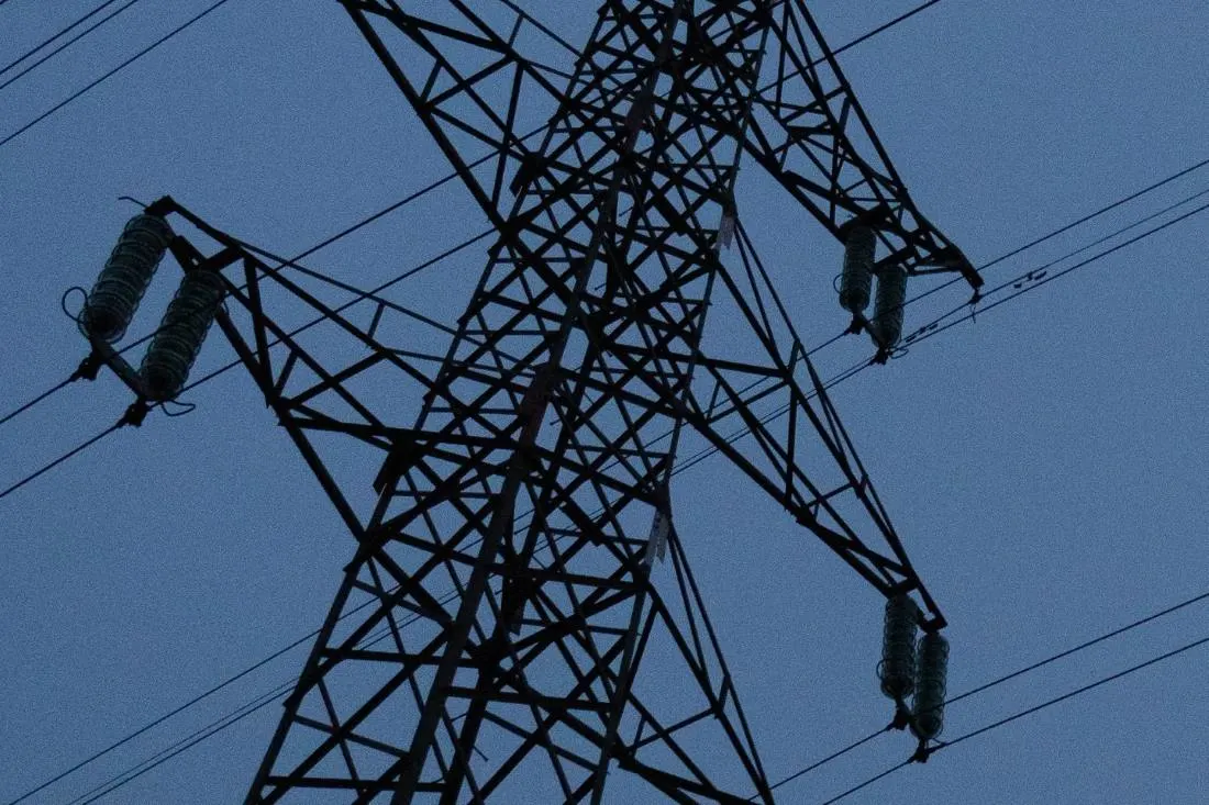 Nagyfeszültségű távvezeték fémből készült tartóoszlopa sziluettként a sötétkék, szürkületi égbolt előtt, feszítőszigetelőkkel.