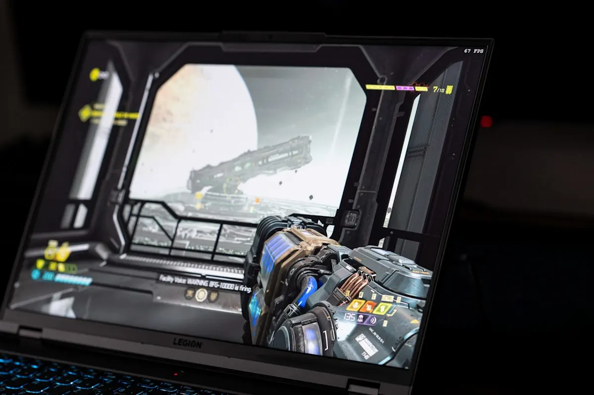 Lenovo Legion laptop kijelzője, amin a Doom Eternal játék fut belső nézetből egy futurisztikus fegyverrel és 67 FPS számlálóval.