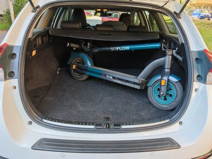 Egy autó nyitott csomagtartójában keresztben elhelyezett, kék és fekete színű, összecsukott SoFlow SO4 Pro Gen 2 elektromos roller látható.