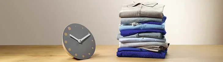 Szürke óra arany pöttyökkel és egy halom kék-szürke összehajtogatott ruhát mutat a kép.