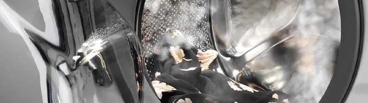 Ezüstös mosógép, benne fekete ruha, sárga mintákkal, vízpermettel.