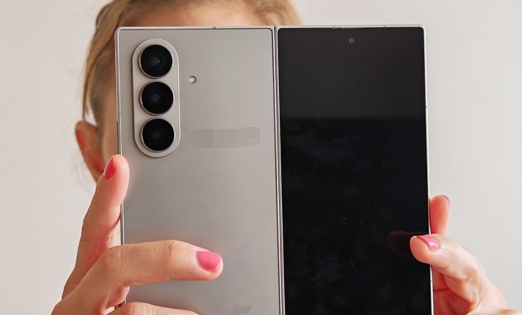 Kihajtott Samsung Galaxy Z Fold okostelefon elölnézetből, kézben tartva, látható háromkamerás hátlapi modullal.