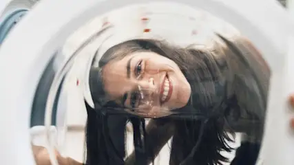 Innenansicht einer weißen Waschmaschinentrommel mit lächelnder Person, die hineinschaut.