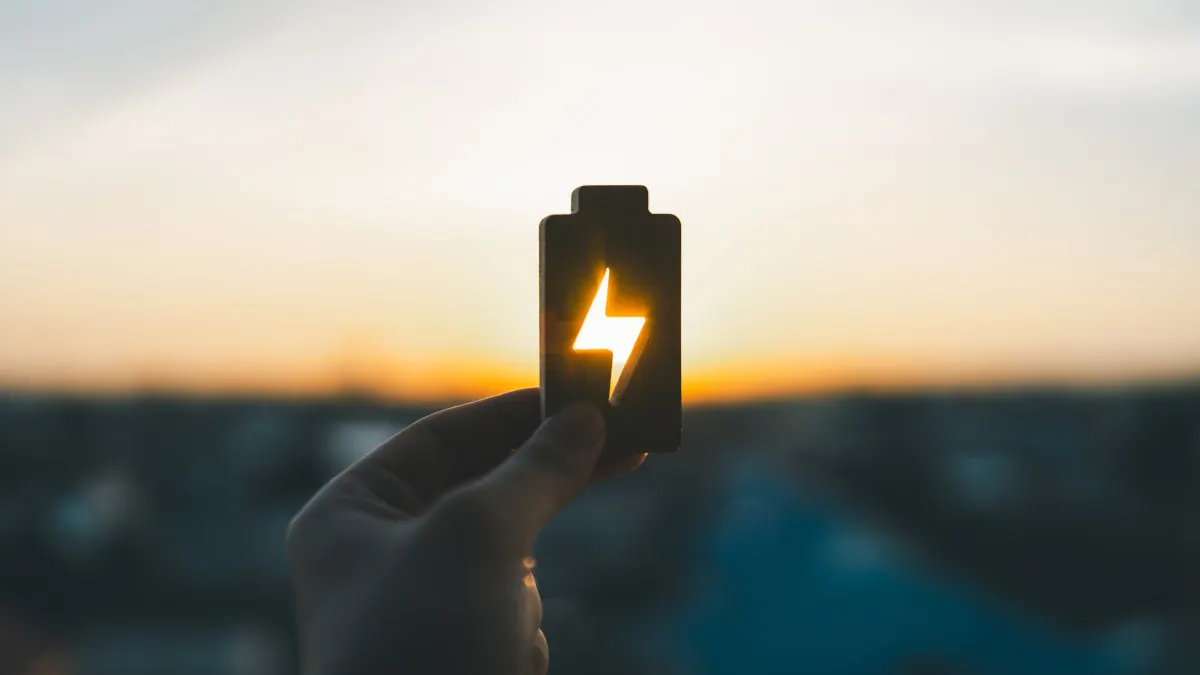Eine Hand hält eine Batterie-Form mit einem Blitzsymbol vor einem hellen, verschwommenen Hintergrund.