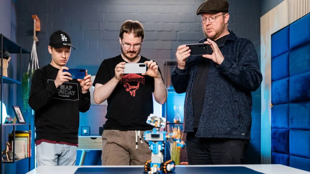 Die TURN ON Kollegen Alex, Michael und Andreas fotografieren einen Modellroboter mit ihren Test-Smartphones.