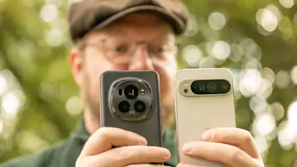 Eine Person hält zwei Mobiltelefone mit Kameras in der Hand, der Hintergrund ist unscharf.