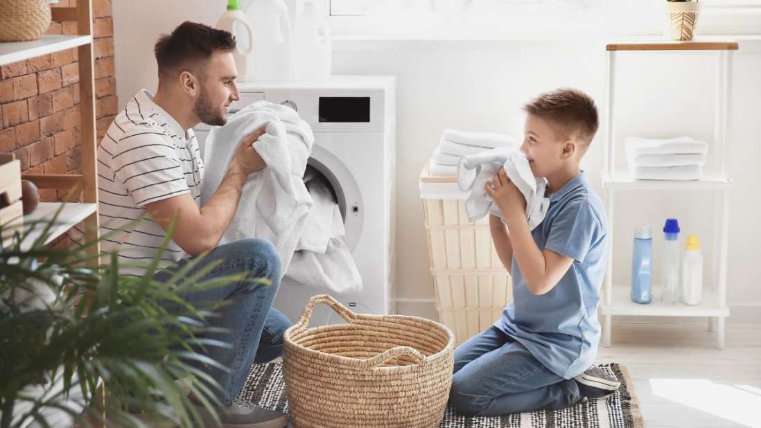 Ein Mann und ein Kind sitzen vor der Waschmaschine und riechen an weißer Wäsche.