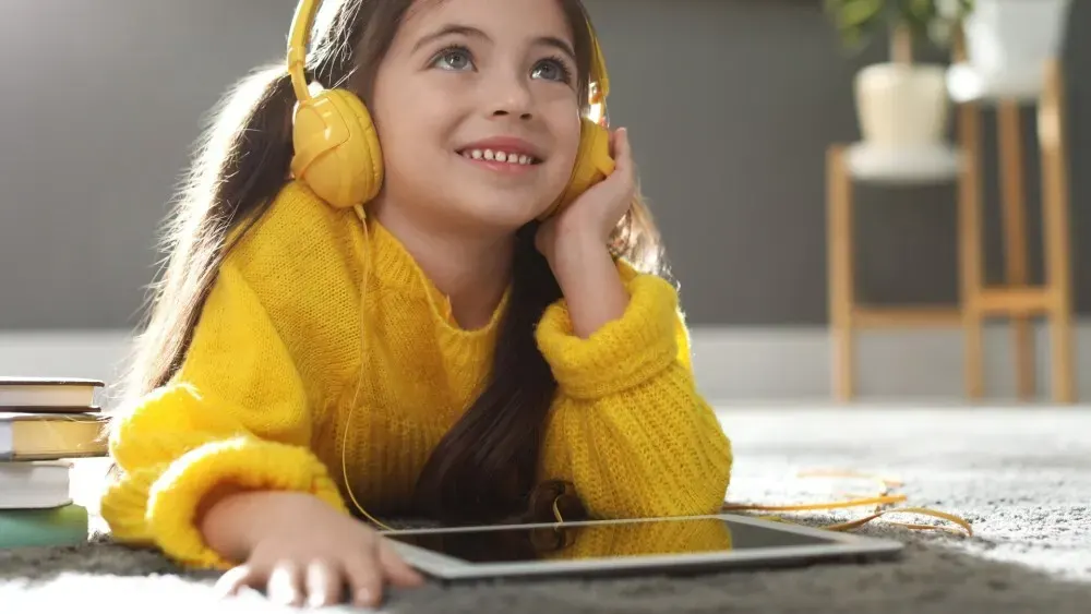Ein Mädchen liegt auf dem Boden und hört mit Kopfhörern Musik von einem Tablet.